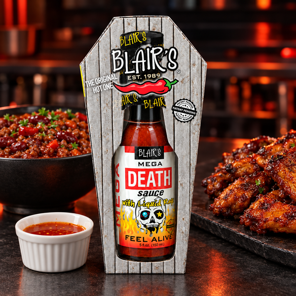 A 150m bottle of Blair's Mega Death Sauce in  a coffin-shaped box on a table with a bowl of chilli con carne and platter of chicken wings. Available to buy in Australia.