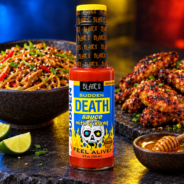 A 150ml bottle of Blair's Sudden Death Sauce with Ginseng on a counter top alongside a bowl of noodles and a platter of chicken wings. Available to buy in Australia.